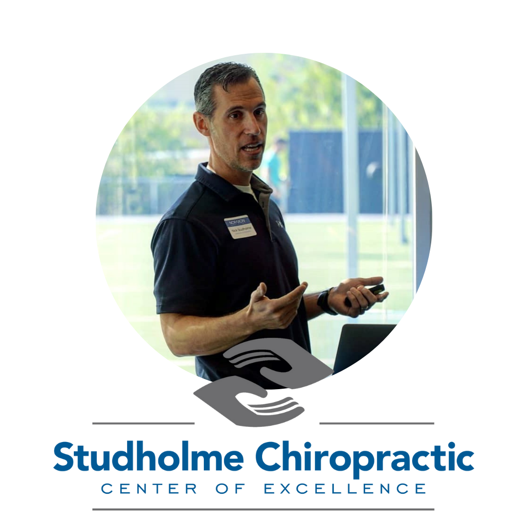 Headshot of Dr. Nick Studholme Headshot of Dr. Nick Studholme, standing and speaking in a professional setting with large windows in the background. He is wearing a navy polo shirt with a name tag and holding a presentation clicker. Below the image is the logo for 'Studholme Chiropractic Center of Excellence,' featuring two interlocked hands.