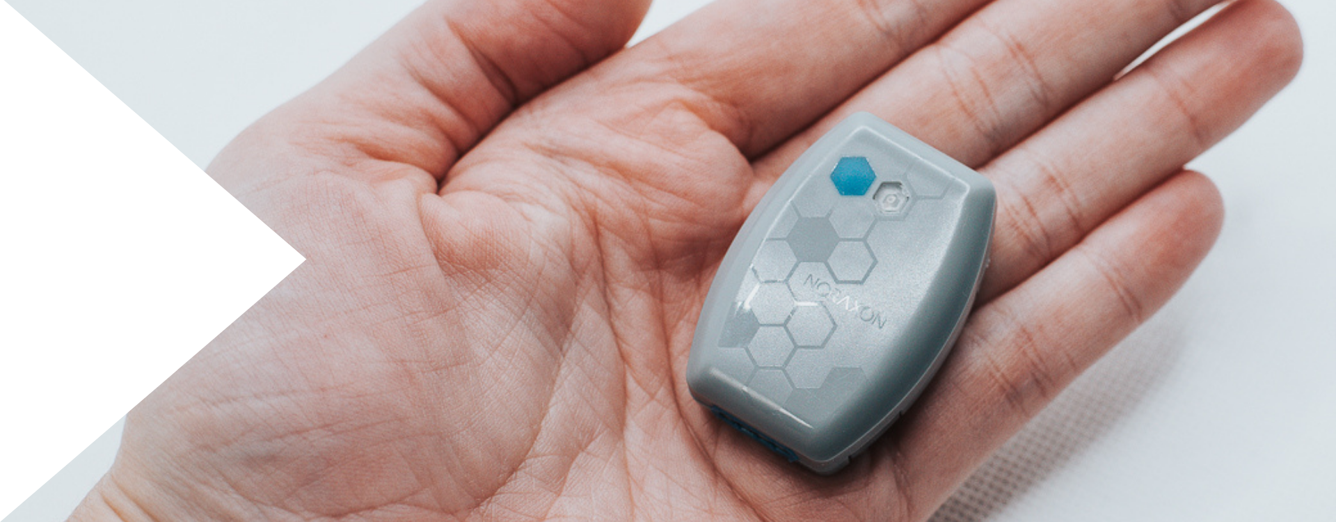 Core EMG in Hands A person holding a small, gray Noraxon Core EMG sensor device in their palm, featuring a hexagonal pattern and a blue indicator on the top.