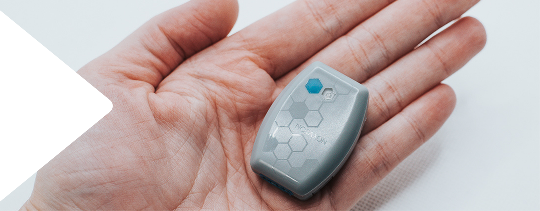 A person holding a small, gray Noraxon Core EMG sensor device in their palm, featuring a hexagonal pattern and a blue indicator on the top.