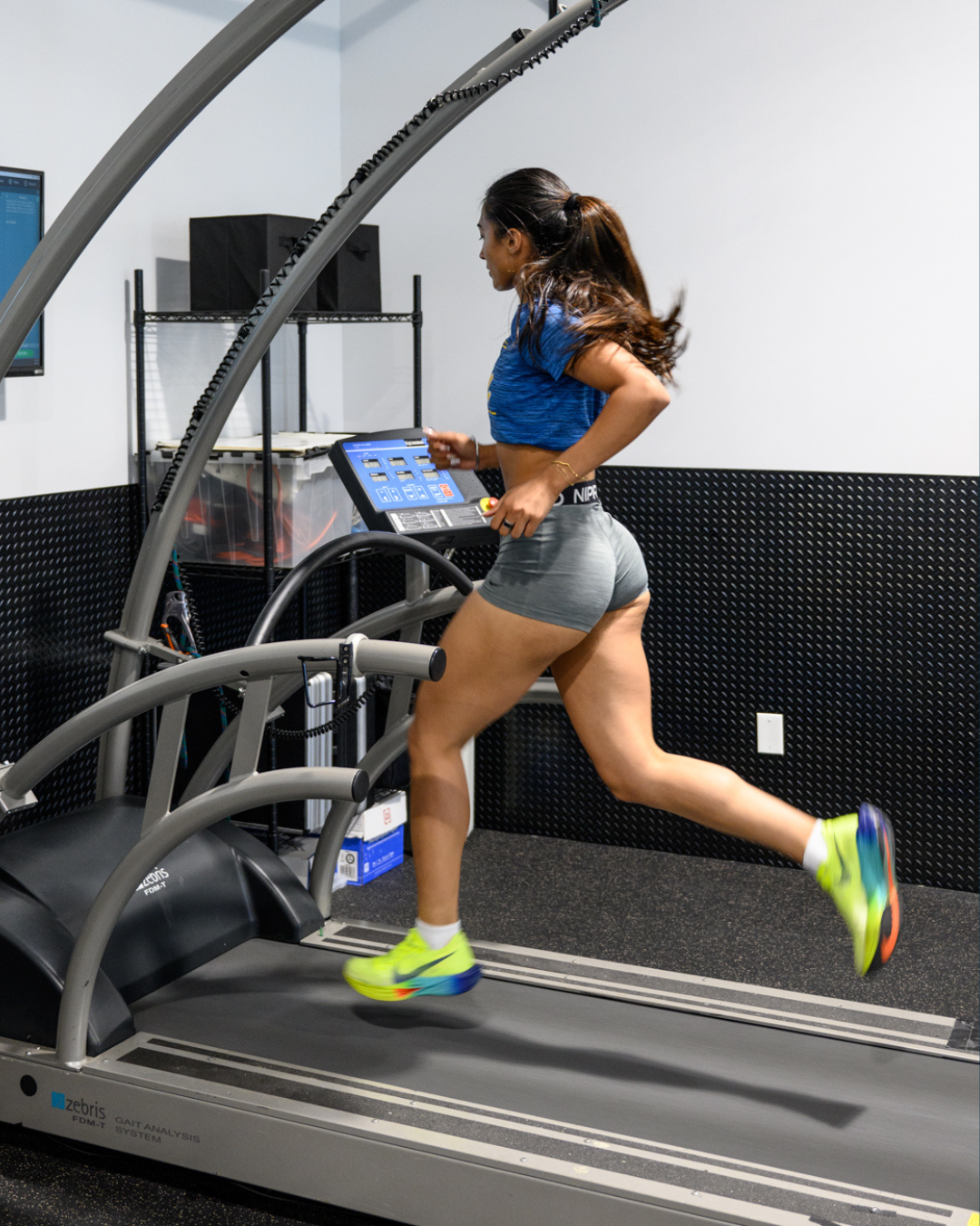 Runner mid-stride on an instrumented treadmill in a biomechanics lab, captured during a gait analysis session.
