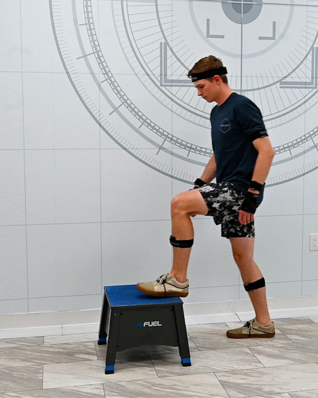 Participant seated in a chair in a biomechanics lab, wearing EMG sensors on the thigh to prepare for a sit-to-stand movement assessment.